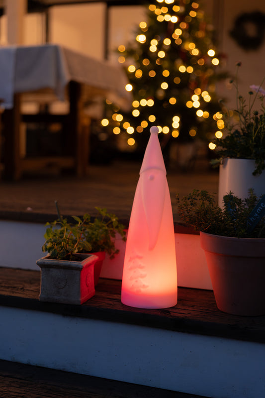 Skinny Santa Solar Light on a wooden step  emitting a red glow with an out of focus Christmas tree in the back ground.