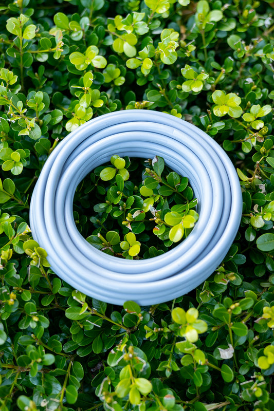 Close-up shot of grey Misting System Extra Hose sitting on top of green hedge