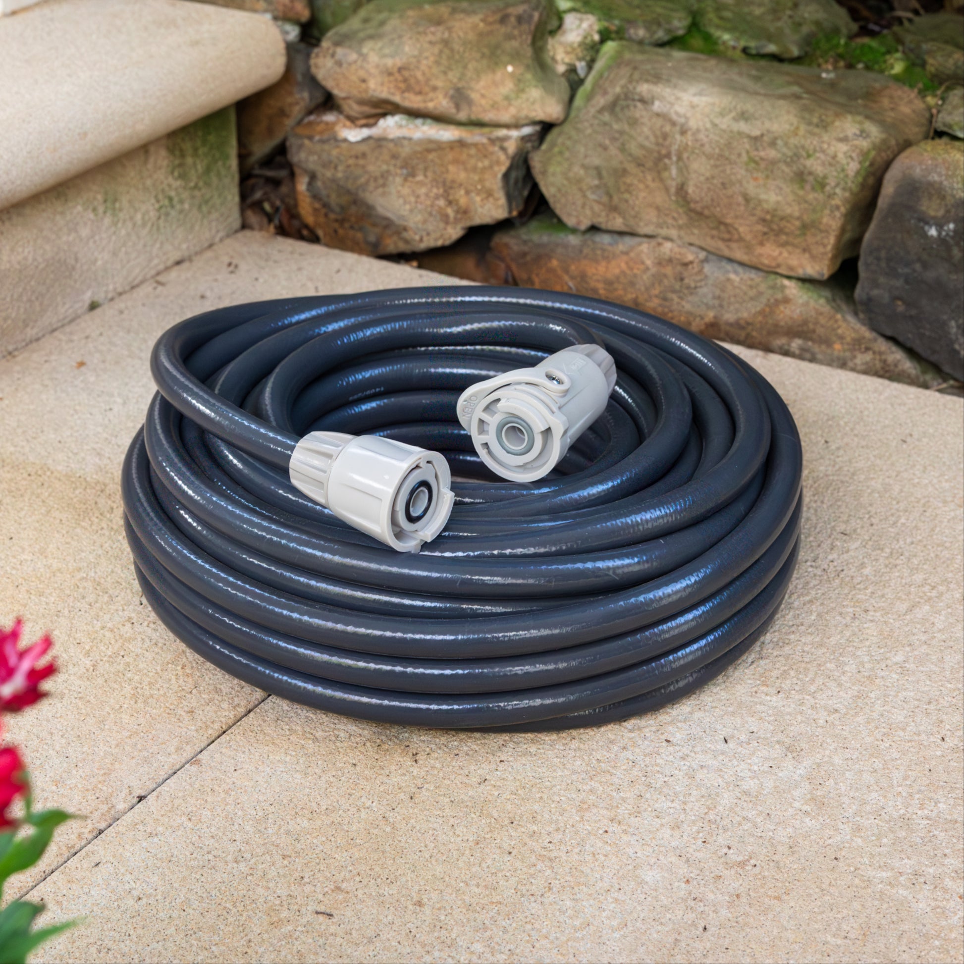Coiled charcoal coloured garden hose with  grey hose fittings on a stone surface