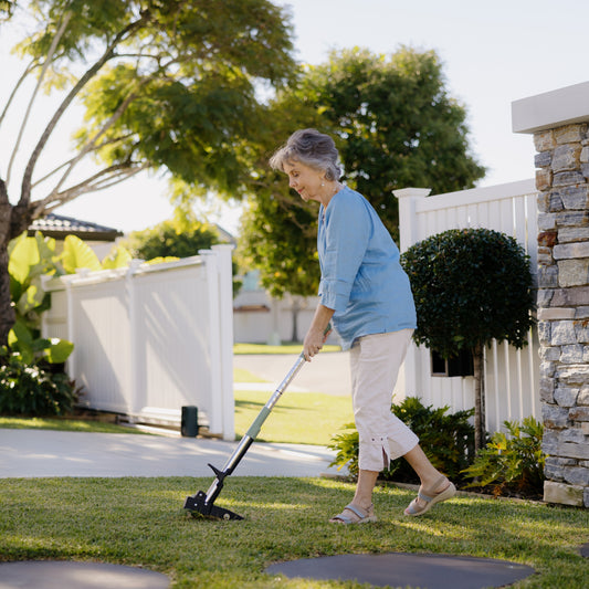 Woman using a stand-up weed puller to remove a weed from lawn in a garden setting