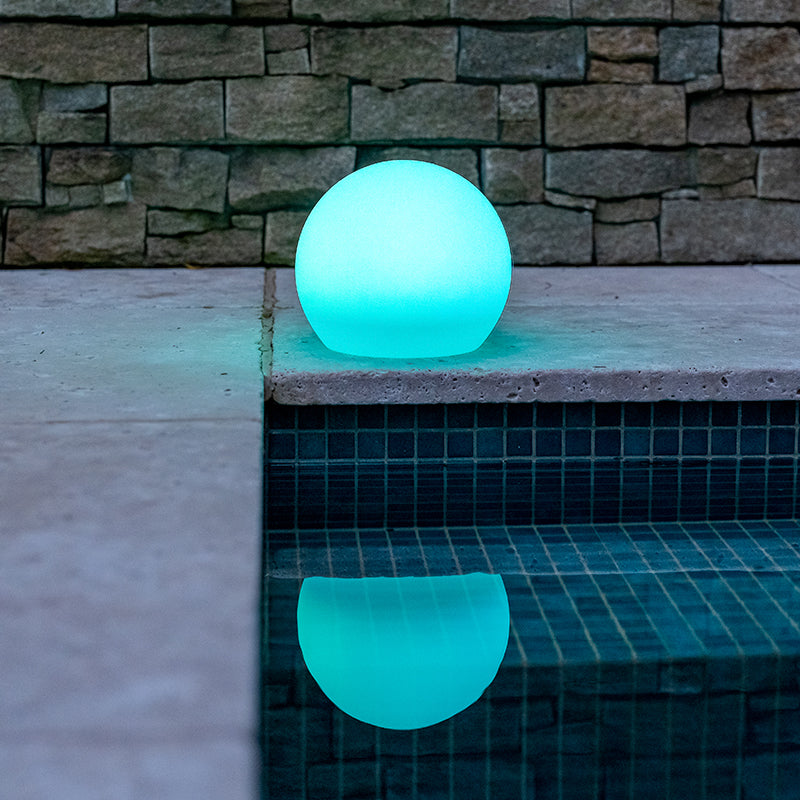 Blue coloured solar sphere light sitting on the edge of a pool. 